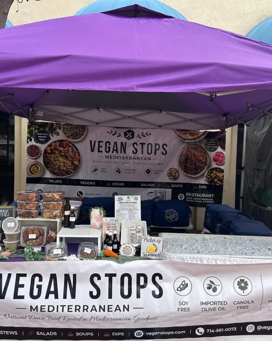 Vegan Stops farmers market booth with Mediterranean meal prep banner